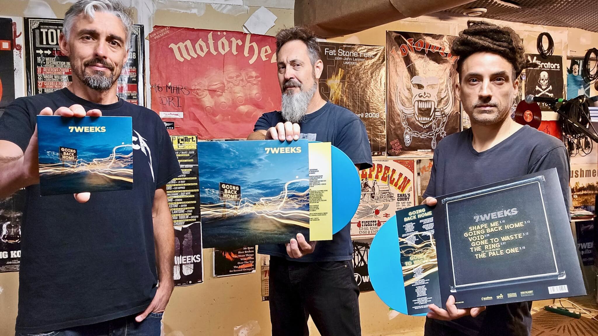 Les trois membres du groupe de rock 7 Weeks présentent les formats physiques CD et vinyle bleu de leur album Going Back Home dans leur studio.