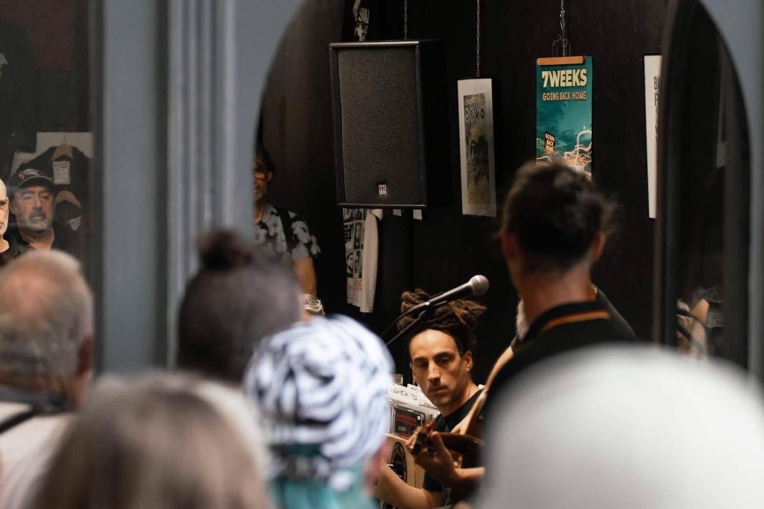 Vue depuis le public du groupe 7 Weeks en concert showcase intimiste avec l'affiche du groupe en fond.