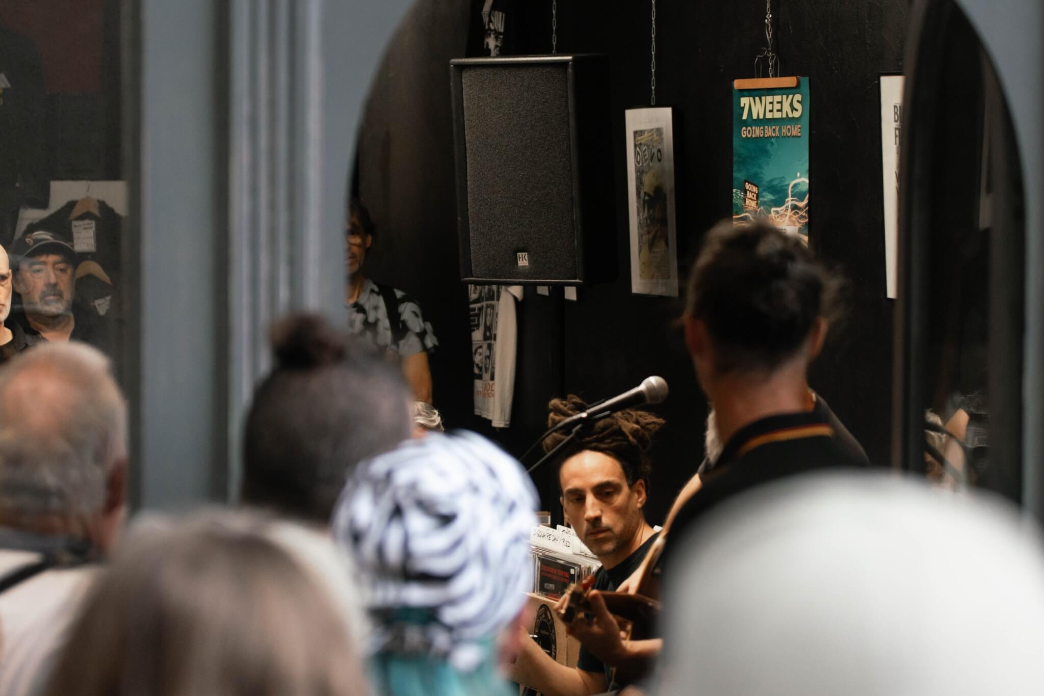 Vue depuis le public du groupe 7 Weeks en concert showcase intimiste avec l'affiche du groupe en fond.